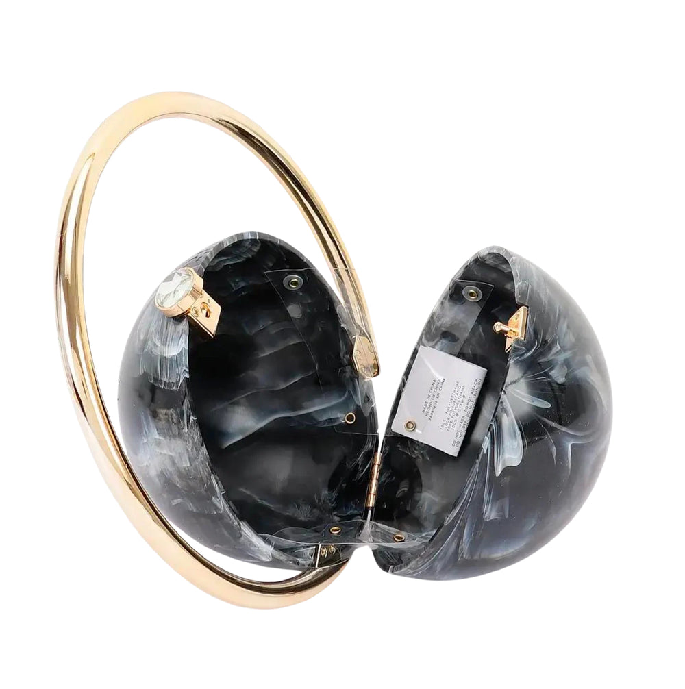 A split-hem clutch bag made of black and gray marbled resin, held together by a wide, polished gold-tone metal arch. A small gold clasp and a white product tag are visible on the inside of the halves.